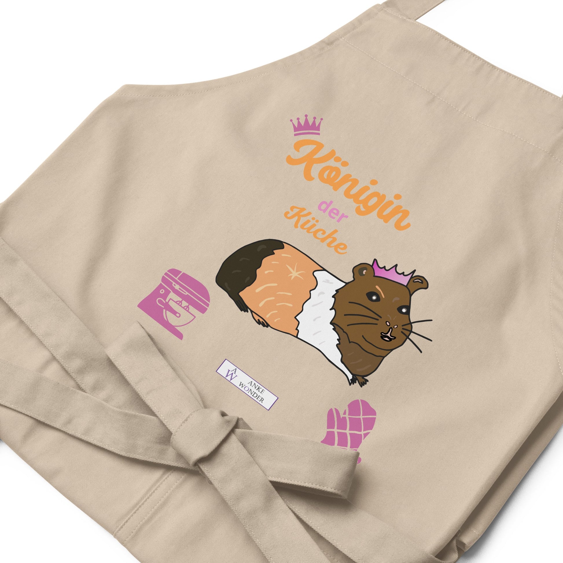 A flat-lay of the natural apron displaying the detailed guinea pig design and “Königin der Küche” typography with Anke Wonder Branding.