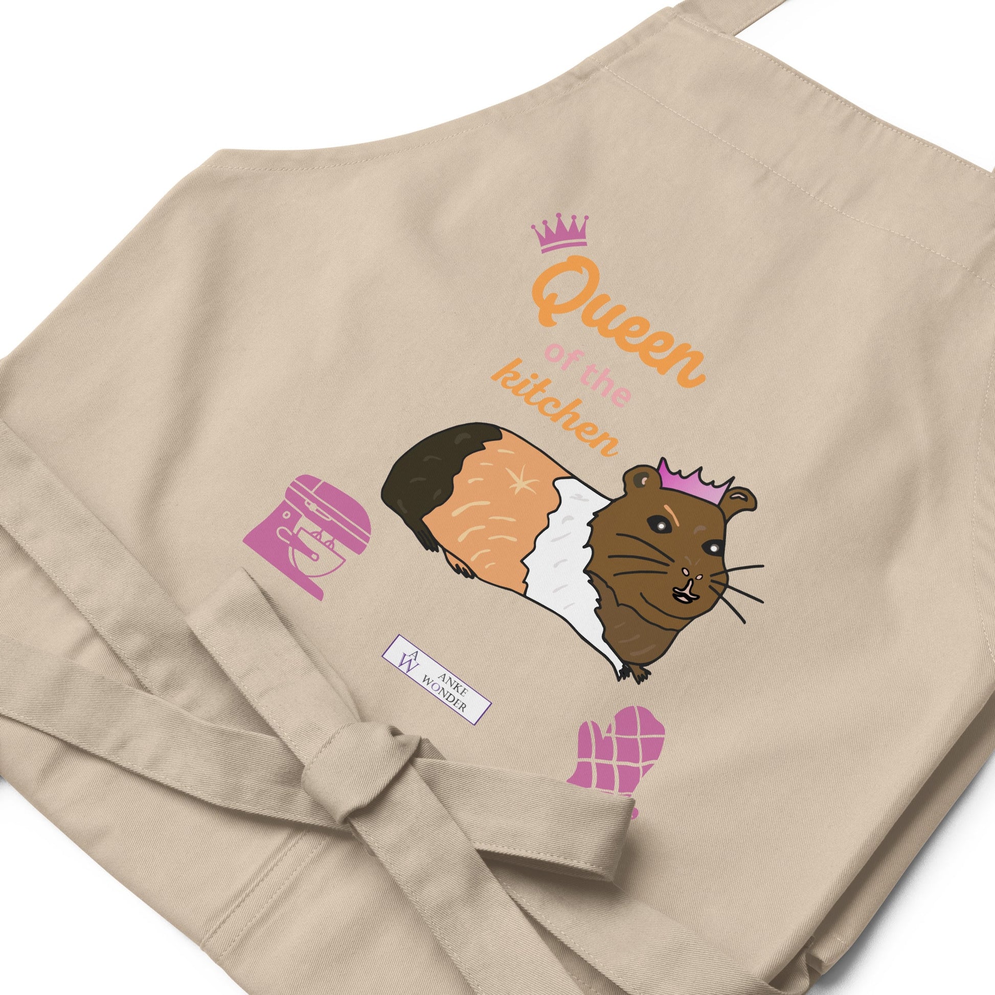 A flat-lay of the natural apron featuring the guinea pig in a pink crown and fun typography spelling “Queen of the Kitchen and the Anke Wonder branding.