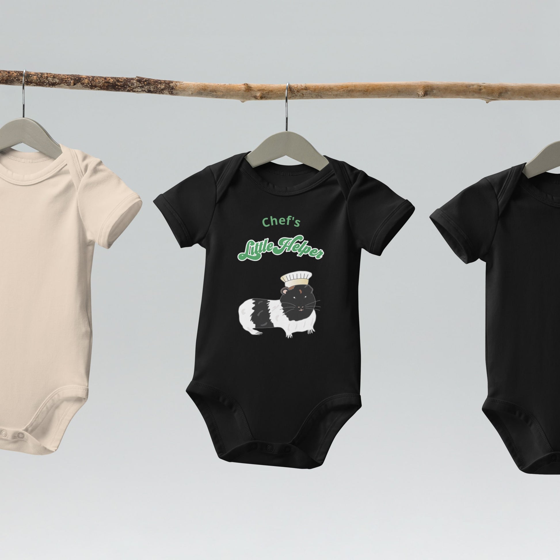 Eco-friendly black baby bodysuit with a cute guinea pig chef design, hanging on a wooden hanger.