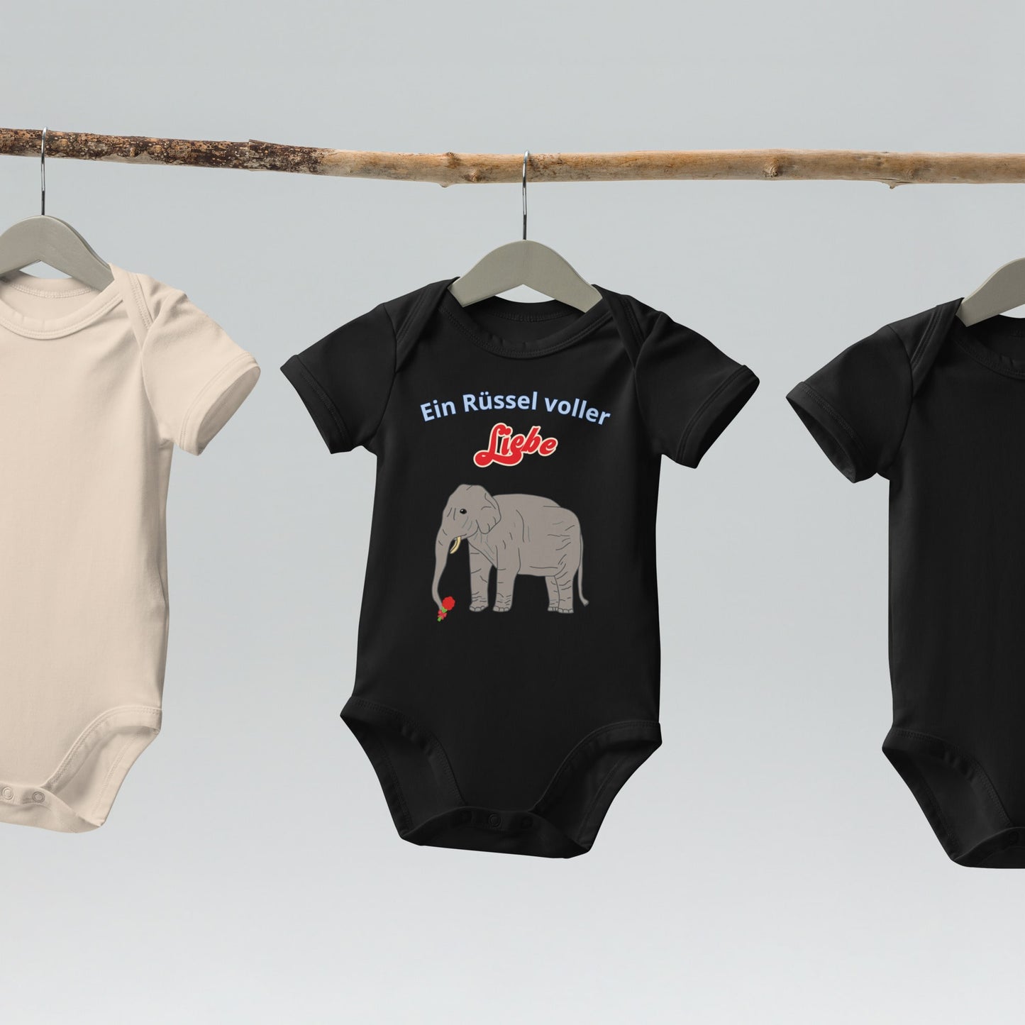  “Ein Rüssel voller Liebe” baby bodysuits with elephant design in black hanging on wooden hangers.
