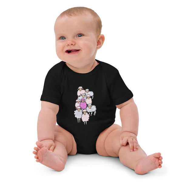 Baby girl sitting while wearing a black organic cotton pink sheep bodysuit, smiling comfortably.