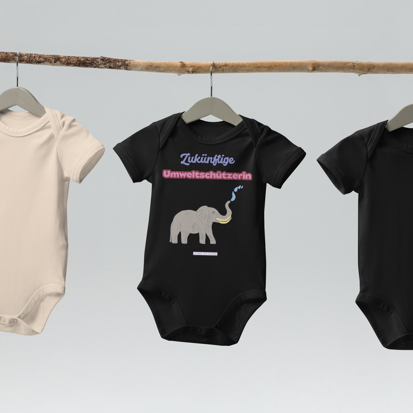 Black baby onesie with elephant graphic and with German slogan “Zukünftige Umweltschützerin” on a hanger against a light gray background