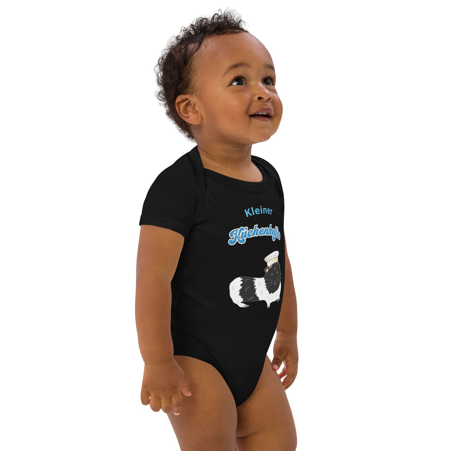 Baby boy wearing an eco-friendly black baby bodysuit with a cute guinea pig chef design, standing to the right.