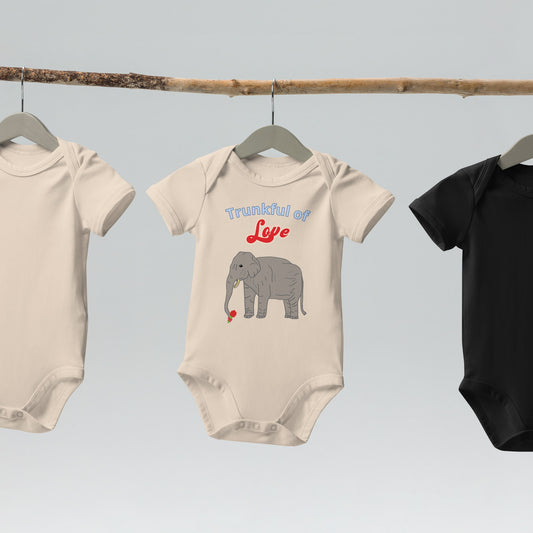 Natural color organic baby bodysuit with an elephant illustration and "Trunkful of Love" text , hanging on wooden hangers.