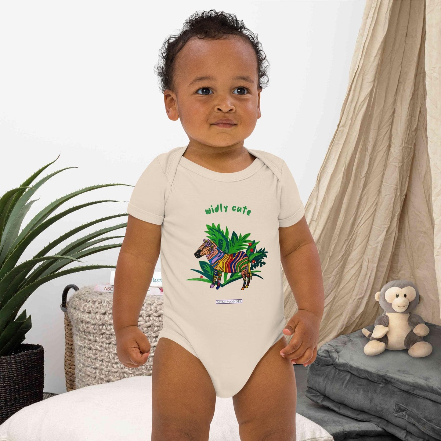 Baby boy wearing a onesie with a colorful zebra design and the words 'widly cute' in a home setting