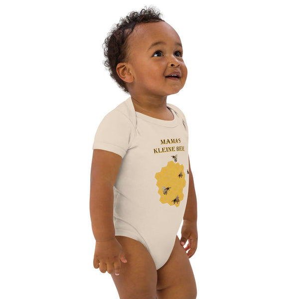 Toddler boy standing slightly to the right, showcasing the front of a natural organic cotton bodysuit with a bee and honeycomb print and German words 'Mama's Kleine Biene'.