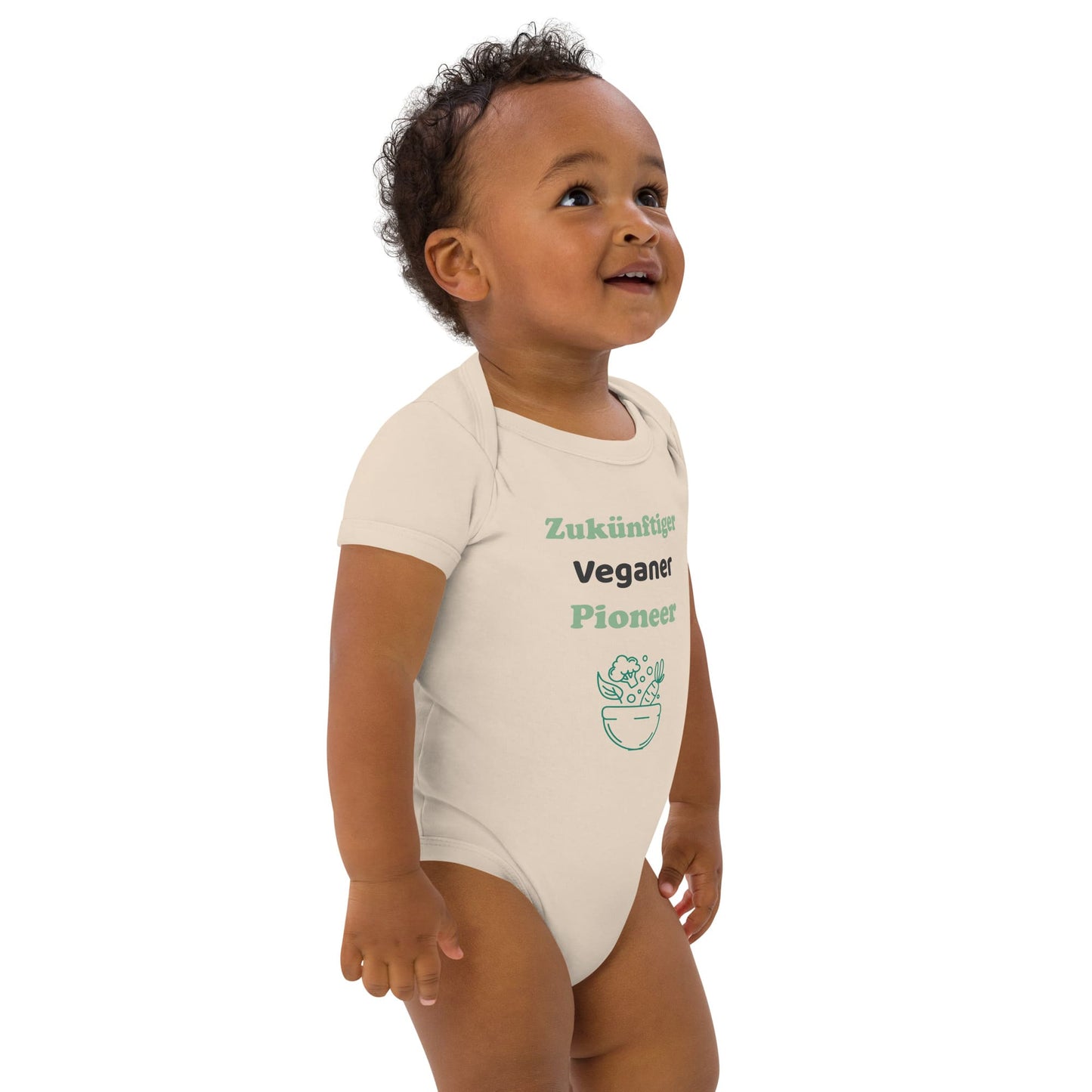 Front right view of a baby boy wearing a natural colored organic cotton bodysuit with "Zukünftiger Veganer Pionier" in green and white text, standing slightly to the right.