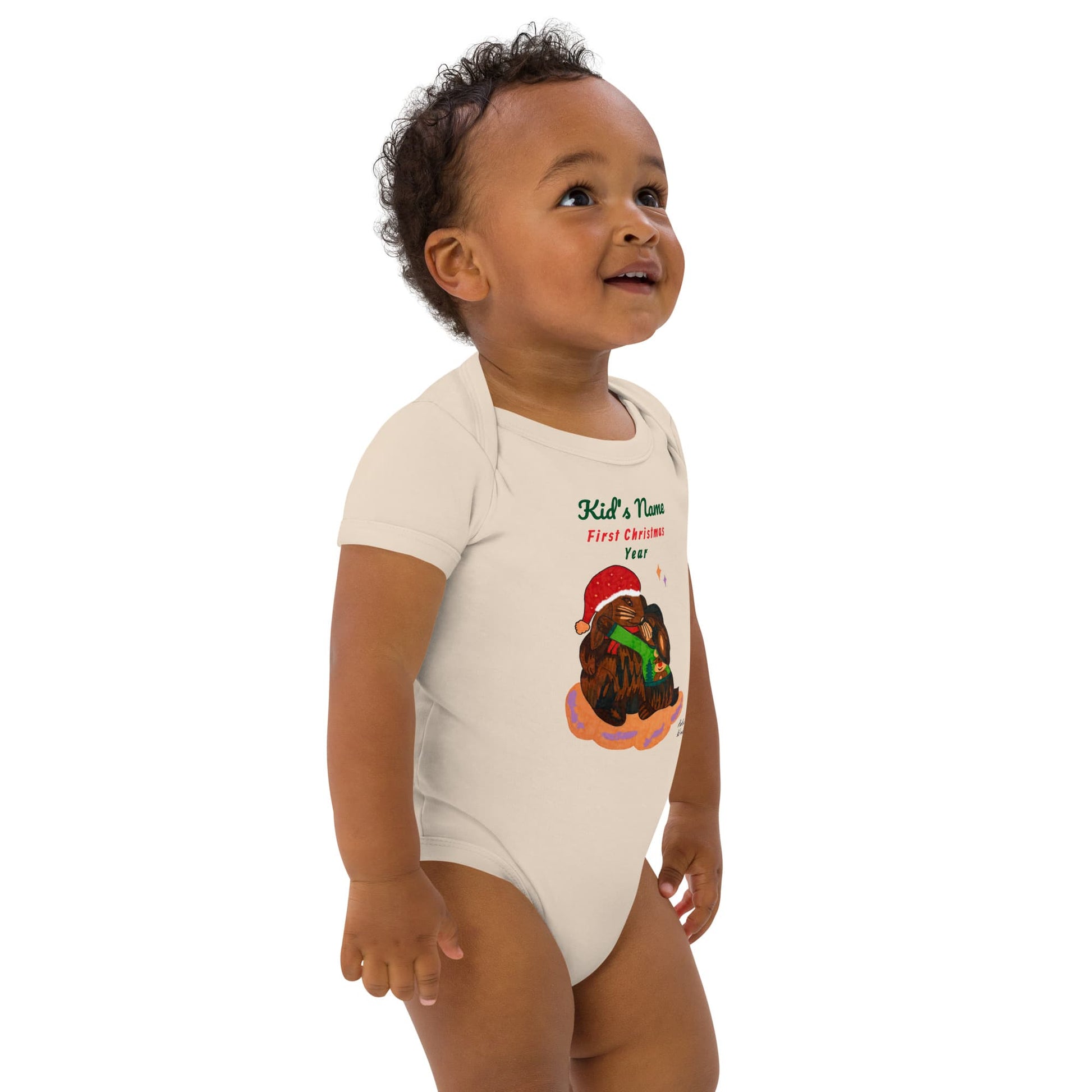 Side view of baby boy wearing a onesie with a Christmas design on a white background