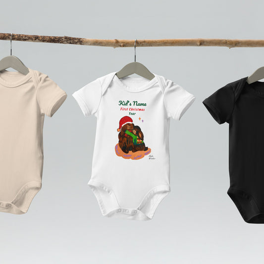 White baby onesies on a rack featuring a Christmas bunny design, saying 'First Christmas'.