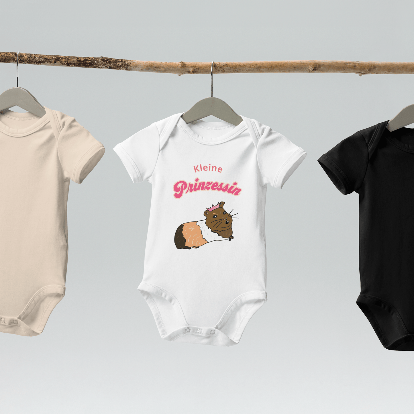 Organic cotton baby bodysuit in white, hanging on a wooden hanger, showcasing a cute guinea pig design with "Kleine Prinzessin" text.