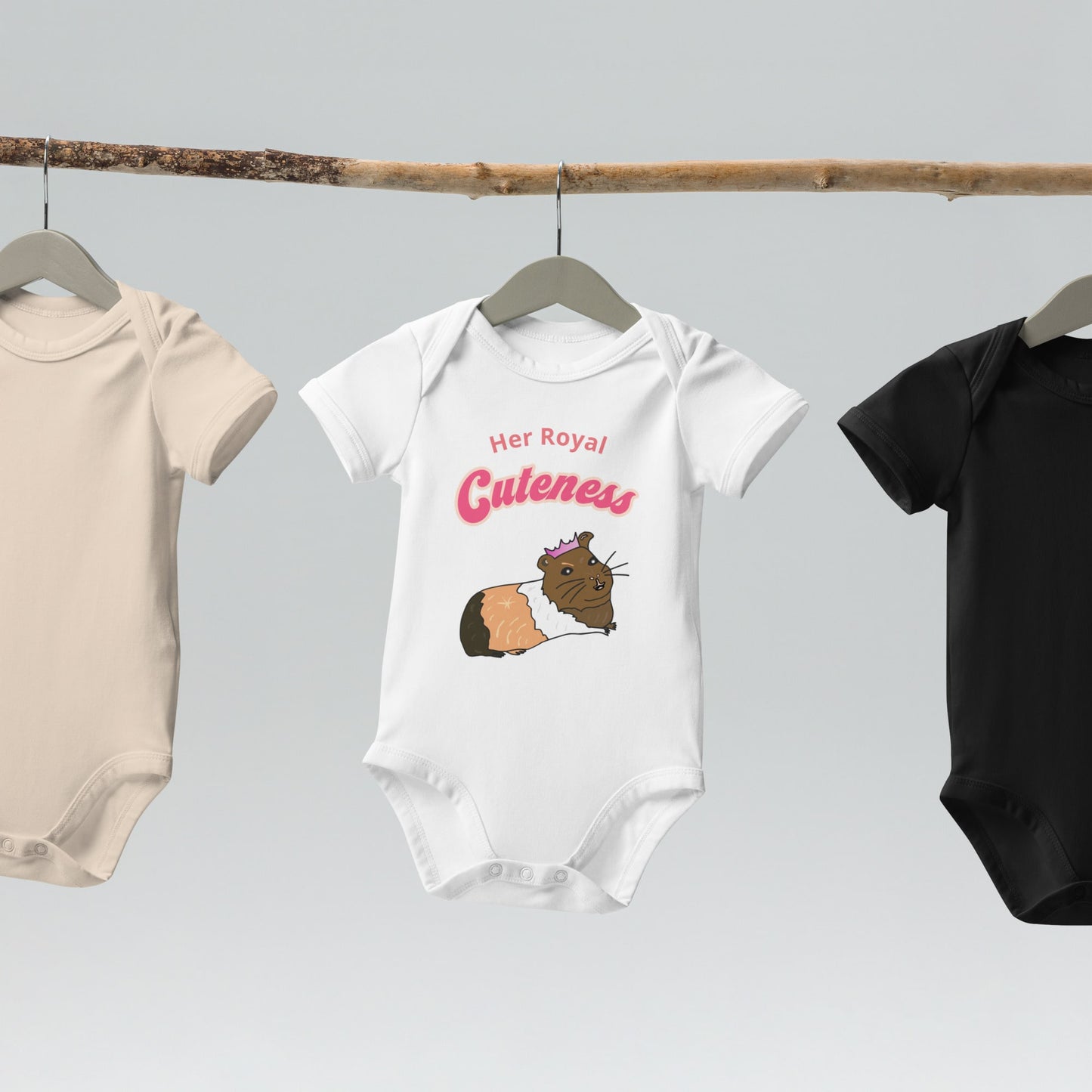 Organic cotton baby bodysuit in white, hanging on a wooden hanger, showcasing a cute guinea pig design with crown.