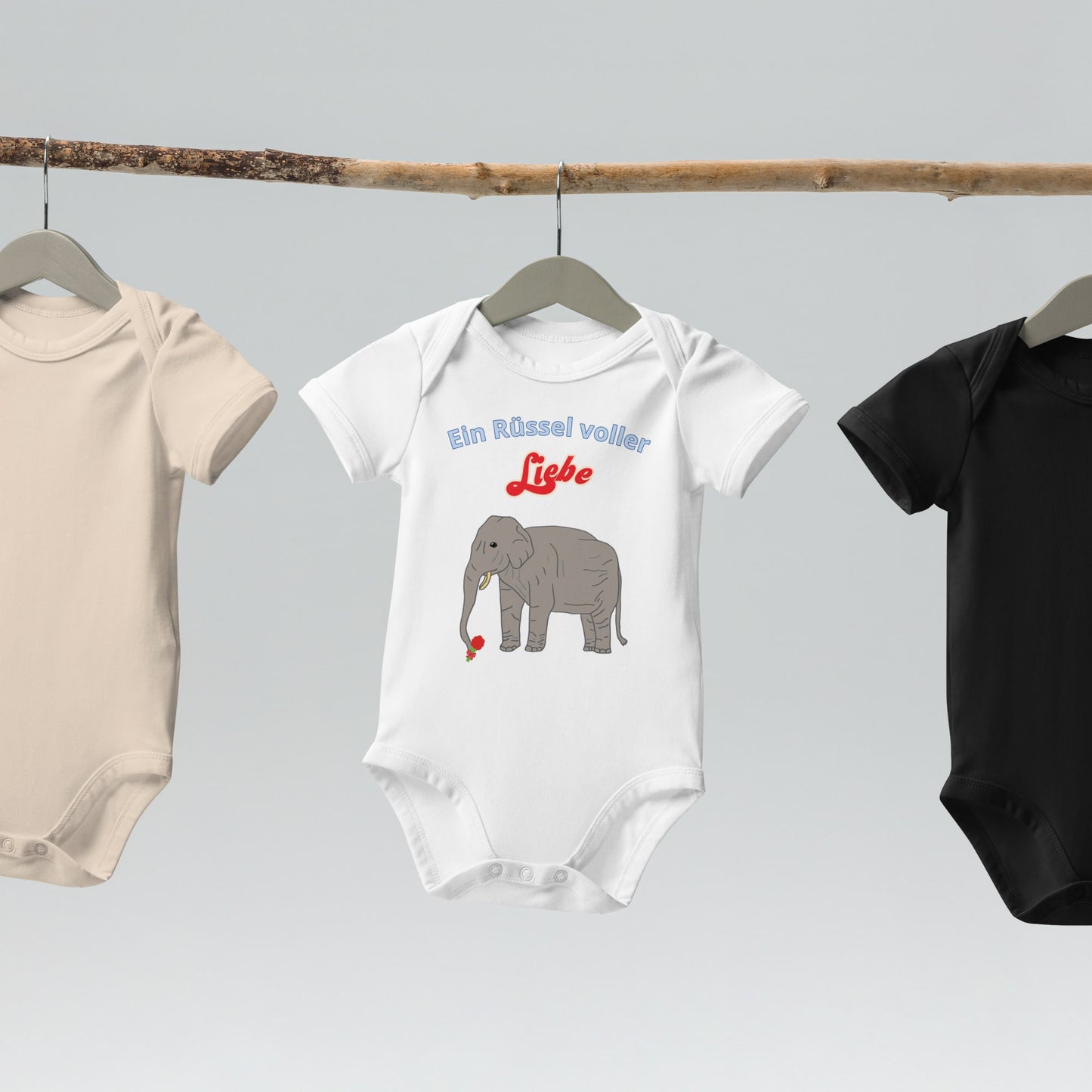  “Ein Rüssel voller Liebe” baby bodysuits with elephant design in white hanging on wooden hangers.