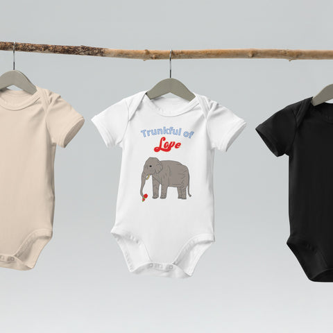 White organic baby bodysuit featuring a sweet elephant design and playful text, hanging on wooden hangers.