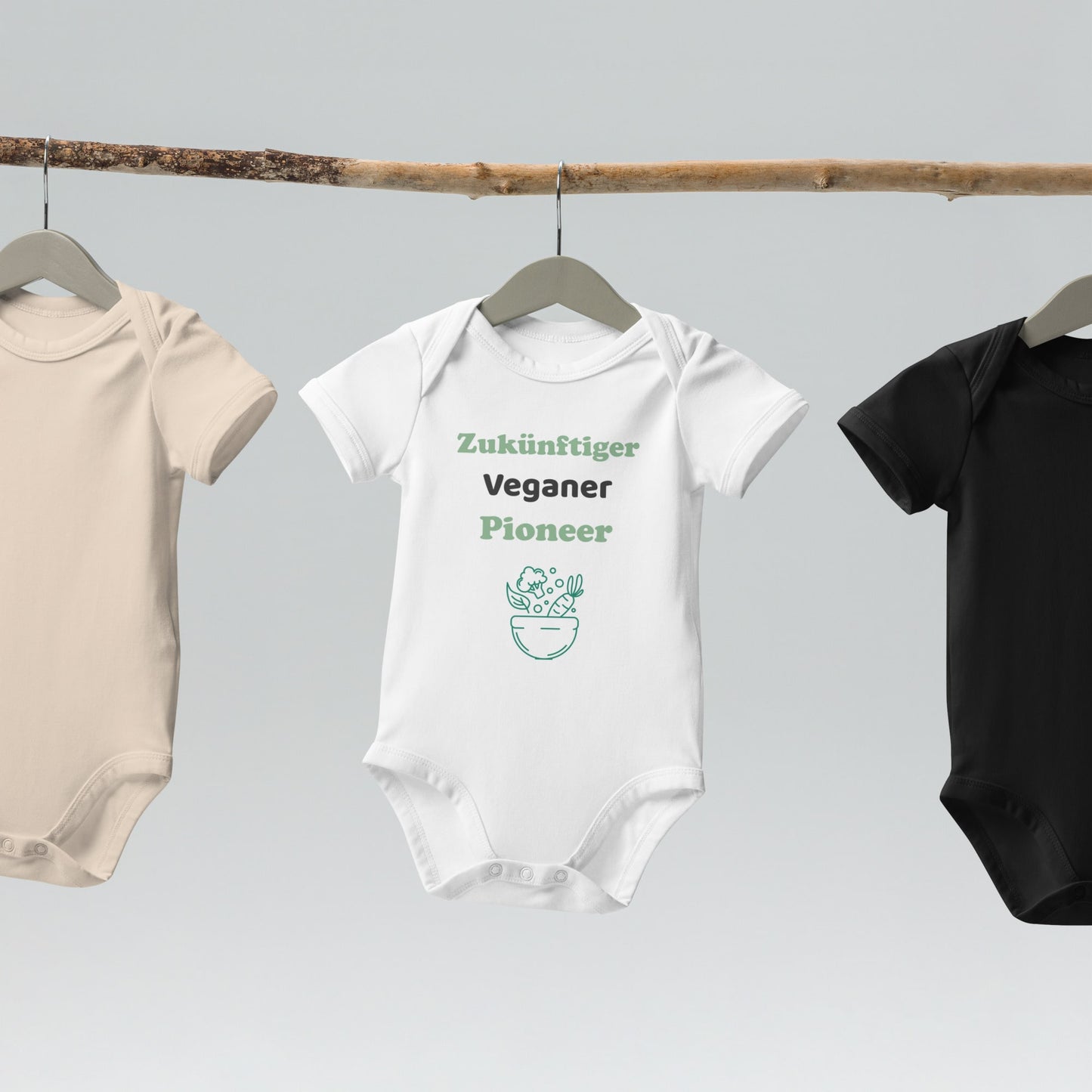  A white organic cotton baby bodysuit with 'Zuküftiger Veganer Pioneer' design hanging on a wooden hanger, showcasing its soft fabric and eco-friendly design.