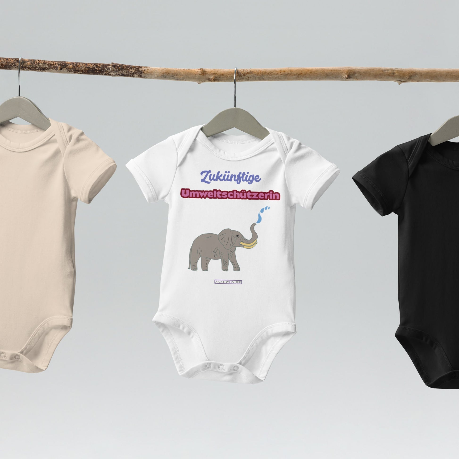 Three baby bodysuits hanging on a rack with German slogan “Zukünftige Umweltschützerin” and elephant design.