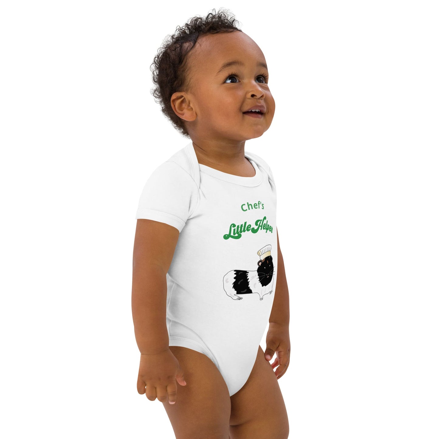 Baby Boy wearing a white bodysuit featuring a hand-painted guinea pig in a chef’s hat with playful green text, standing to the right side.