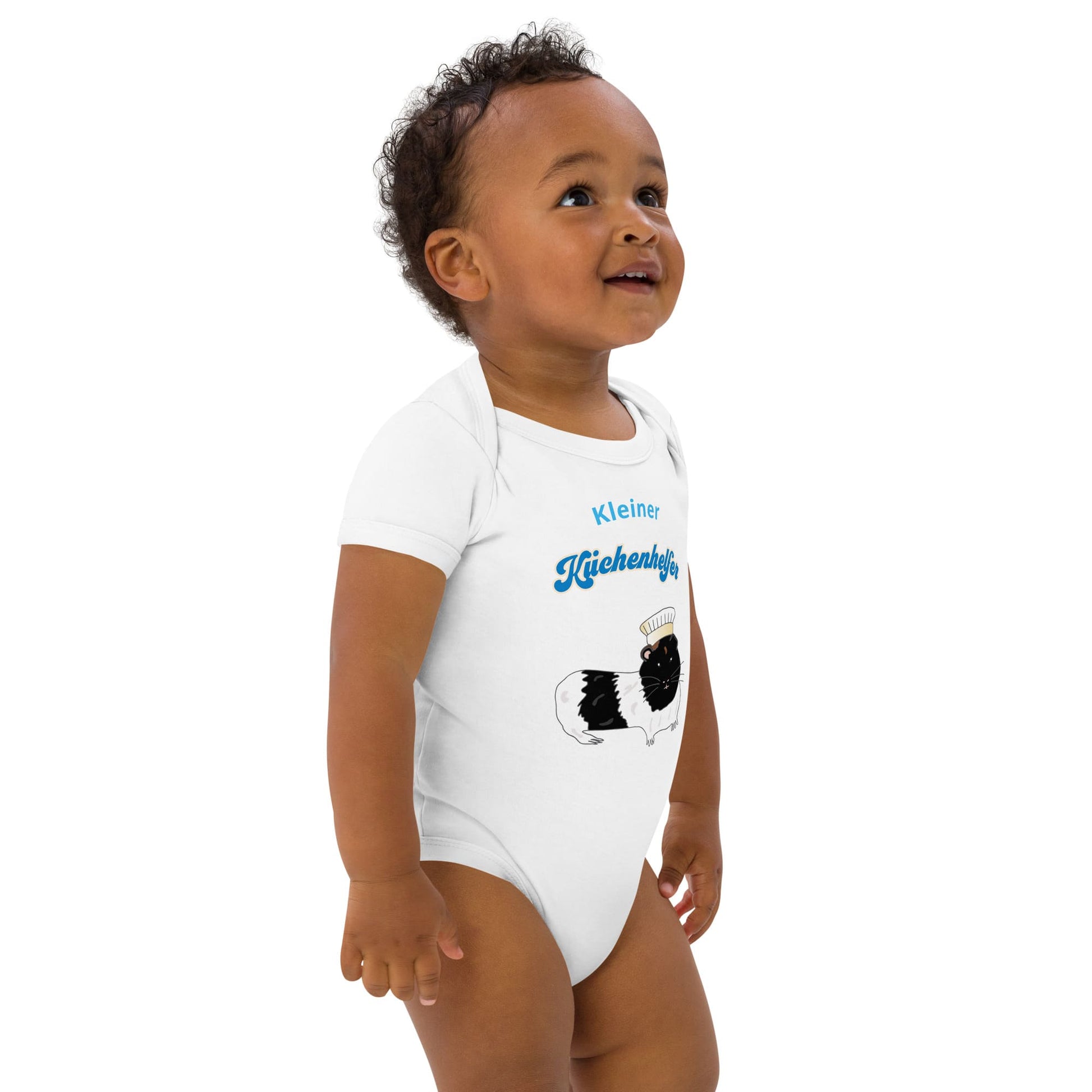 Baby boy wearing an eco-friendly white baby bodysuit with a cute guinea pig chef design, standing to the right.