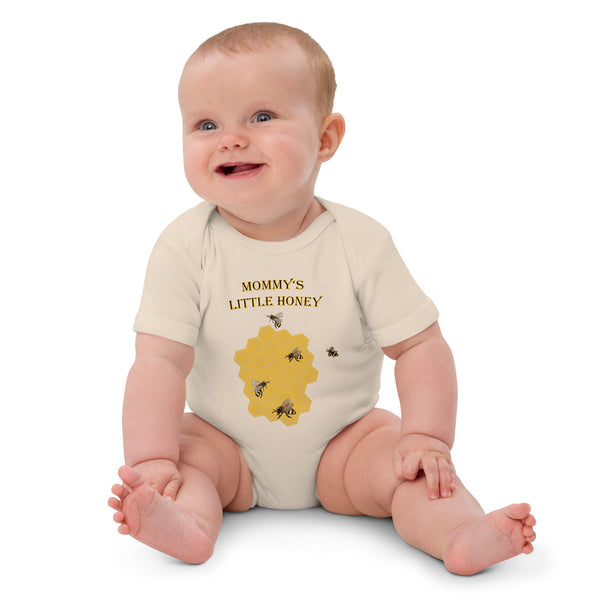 Baby girl sitting while wearing a natural color organic cotton bodysuit, featuring a honeycomb and buzzing bee design.