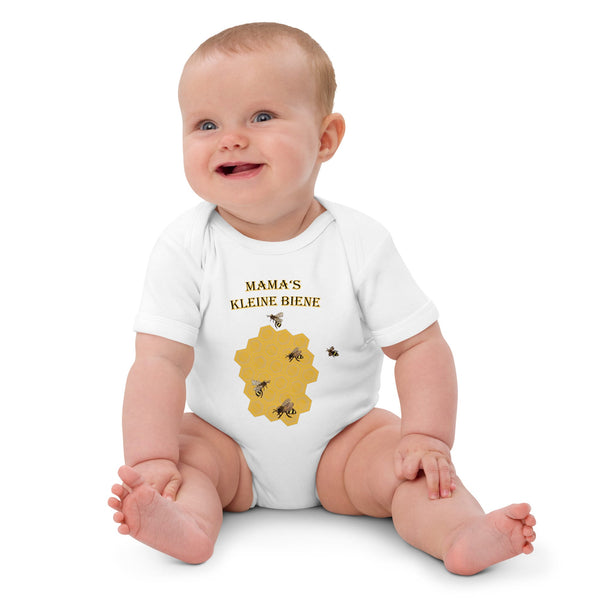 Baby girl sitting while wearing a white organic cotton bodysuit, featuring a honeycomb and buzzing bee design with German words 'Mama's Kleine Biene'.