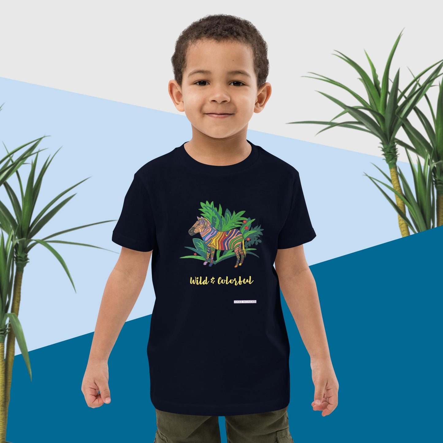 Boy wearing a black t-shirt with a colorful zebra design and text 'Wild & Colorful', standing against a blue and white abstract background with plants.