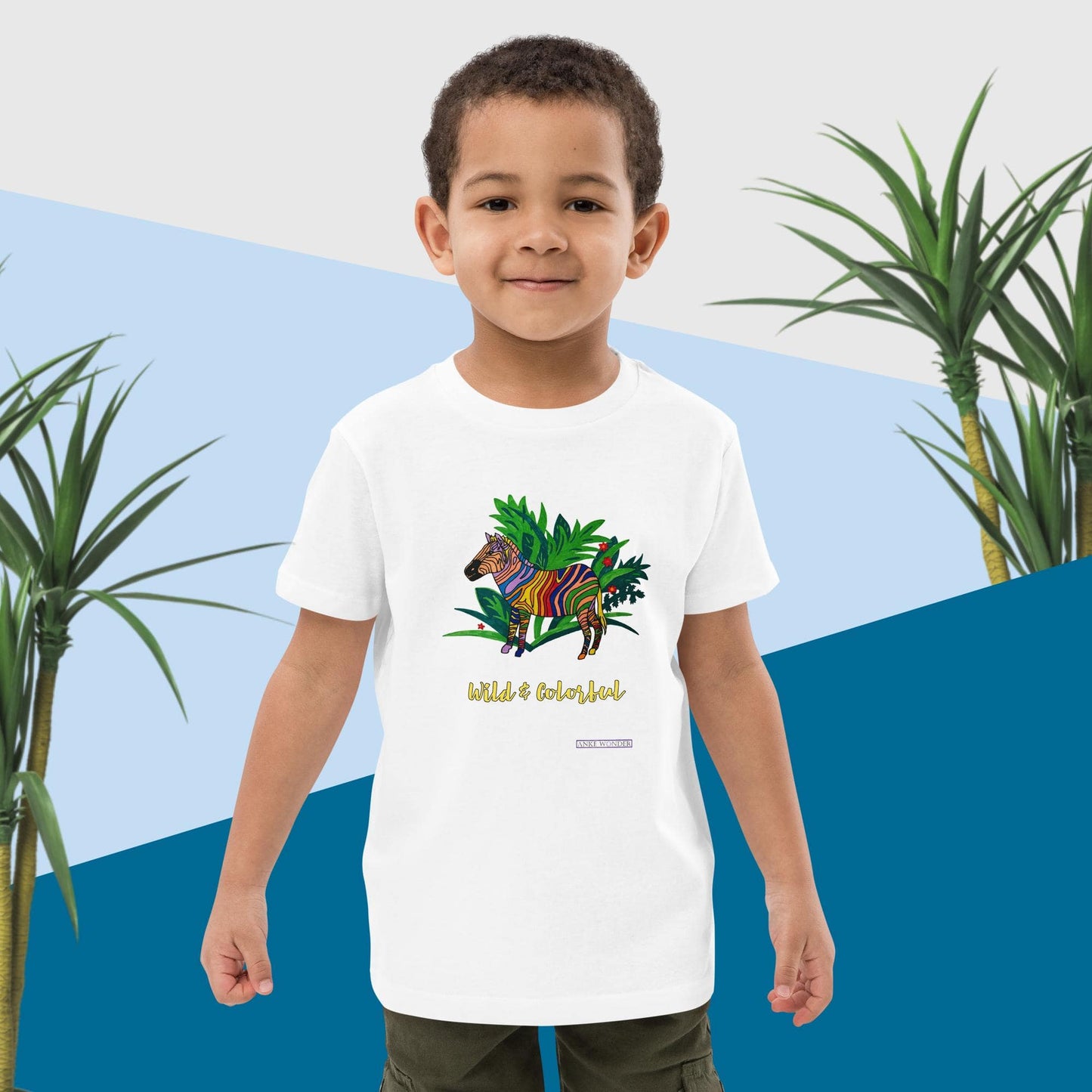 Boy wearing a white t-shirt with a colorful zebra design and text 'Wild & Colorful', standing against a blue and white background with plants.