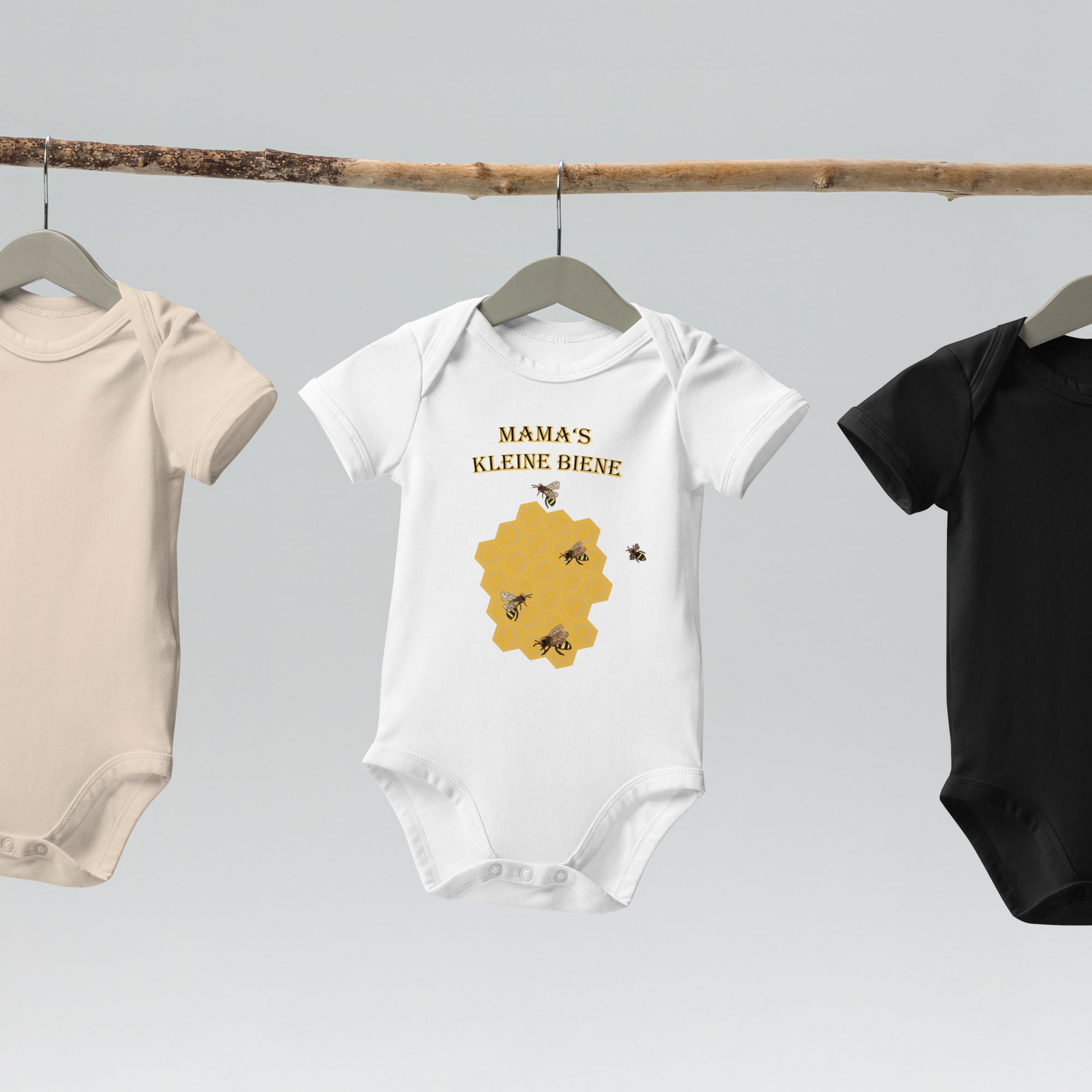 White organic cotton baby bodysuit with a honeycomb and bee design, featuring "Mama's Kleine Biene" text, displayed on a hanger.