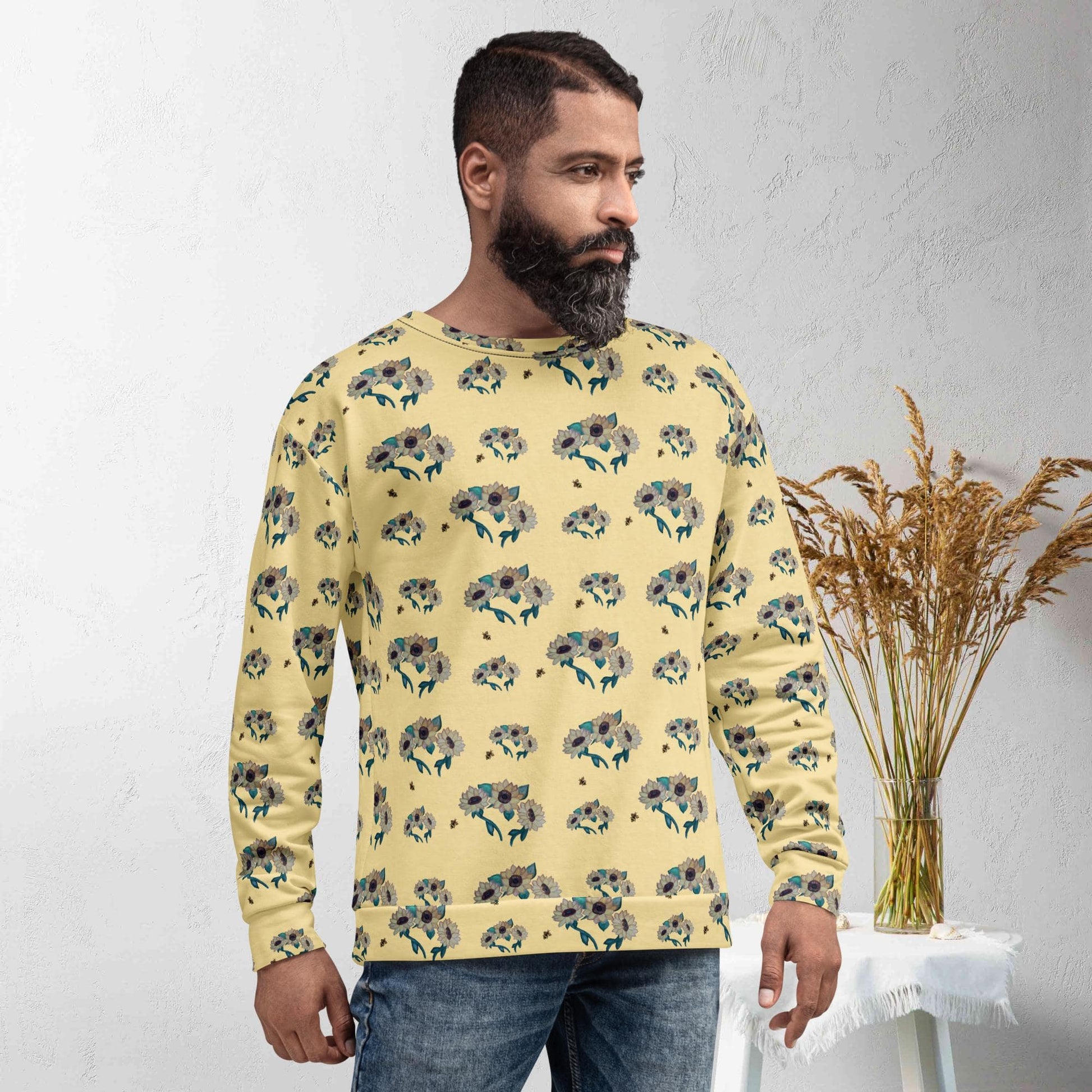 Man wearing a yellow floral-patterned sweater standing against a white wall with a vase of dried plants.