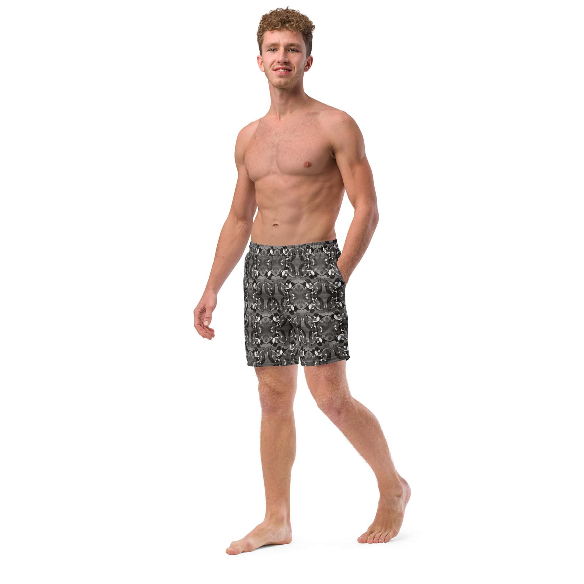 Left side view of men’s swim trunks featuring a mirrored bird art pattern. Recycled fabric, side pocket, and elastic waistband visible.