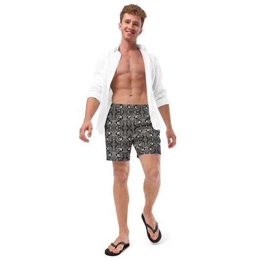 Model wearing black and white bird print swim trunks with a white T-shirt. Sustainable men’s beachwear with artistic design and casual summer style.