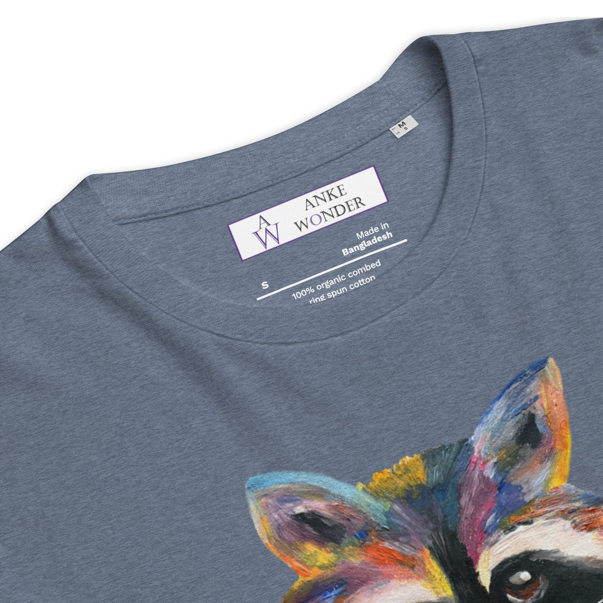 Close-up of a heather slate blue t-shirt by Anke Wonder, featuring a colorful painted raccoon graphic on the front and the brand's inner neck label.