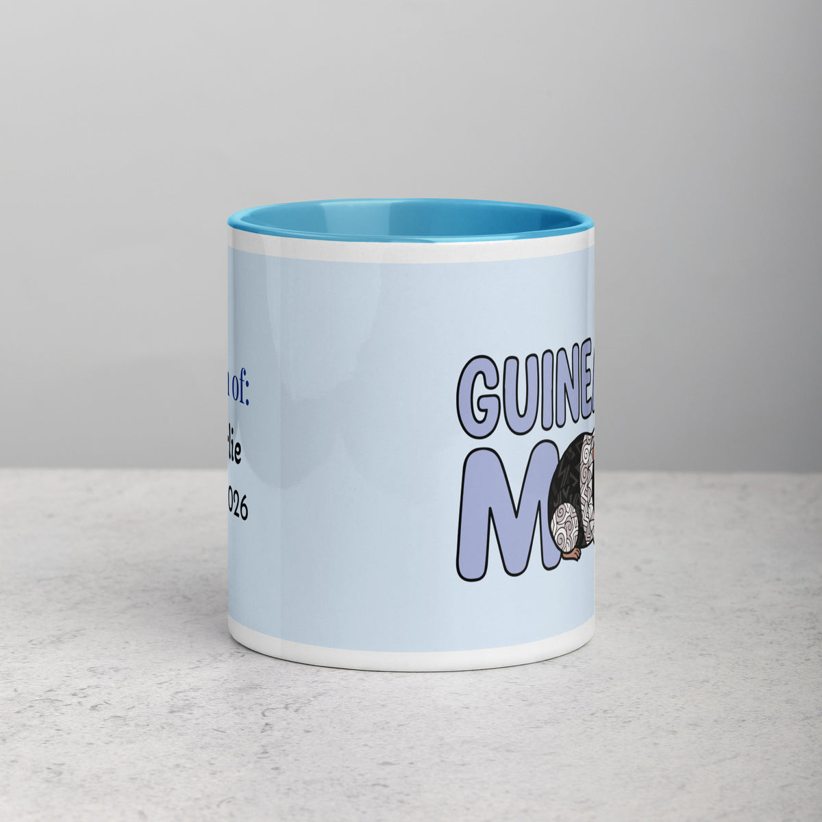 Side view of white and blue ceramic mug with a rblue handle and red interior displaying the words "Guinea Pig Mom" and an illustrated black and white guinea pig.