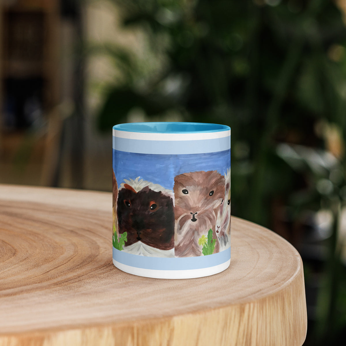 A ceramic mug with a custom illustration of three guinea pigs sitting on a light-colored wooden table, with a blurred green garden background.