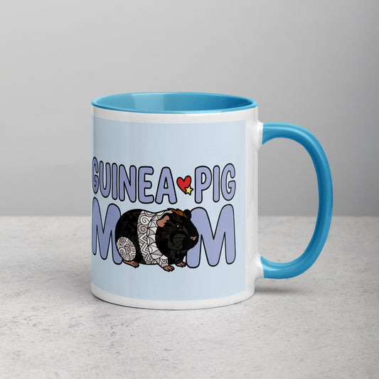 White and blue ceramic mug with a rblue handle and red interior displaying the words "Guinea Pig Mom" and an illustrated black and white guinea pig.