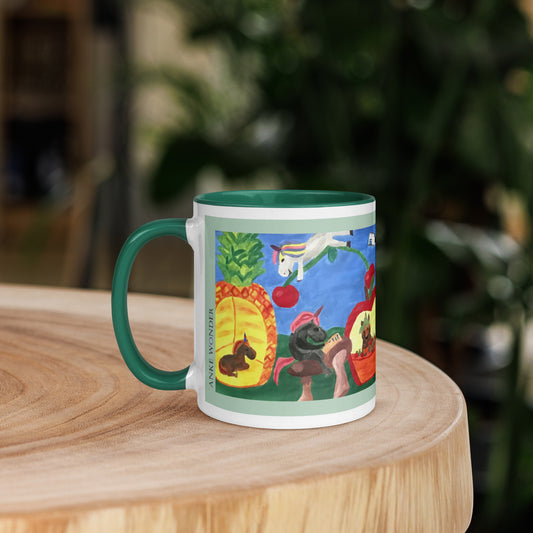 A ceramic mug with a green handle and interior, featuring a colorful illustrated unicorn print, displayed on a round wooden surface with a blurred green background.
