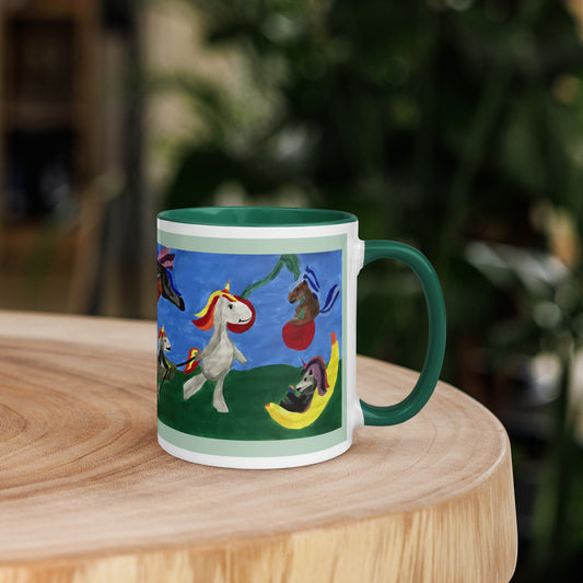 A ceramic mug with a dark green handle and interior, featuring a colorful whimsical illustration of unicorns and other playful animals on a blue sky background, set on a wooden table with a blurred green garden background.