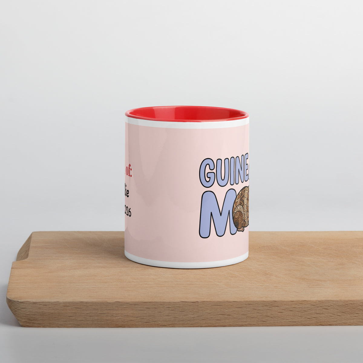 Side view of personalized Guinea Pig Mom ceramic mug featuring a cute brown and white guinea pig illustration with red handle and red interior, held in hands.