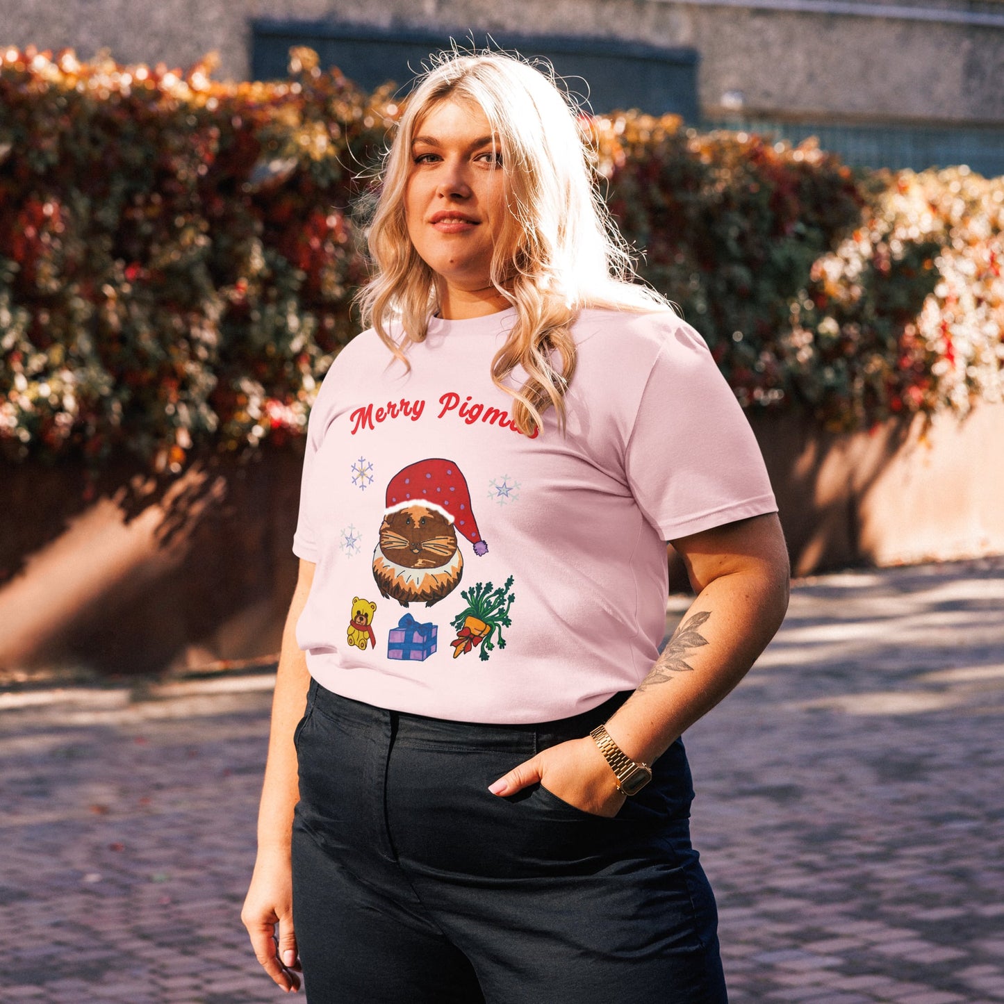 Woman wearing a pink t-shirt with Christmas-themed guinea pig design and text 'Merry Pigmas' outdoors.