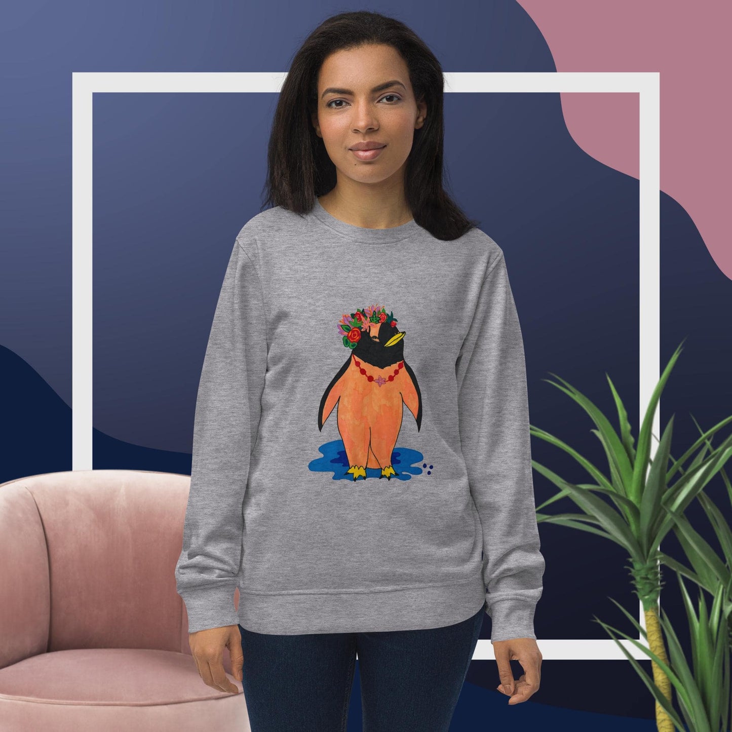 Woman wearing a gray sweatshirt with a penguin design, standing in front of a pink chair and plant.