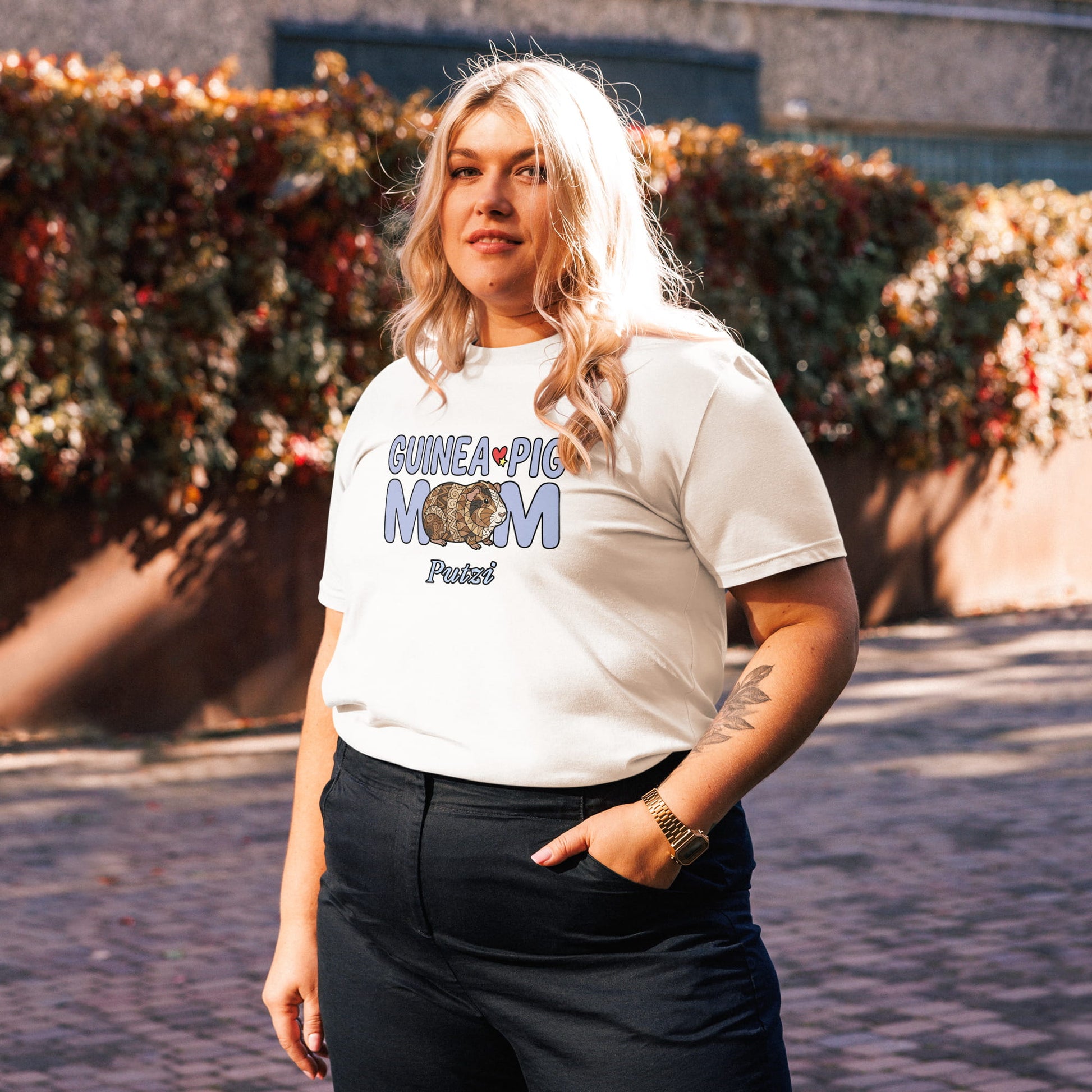 Person wearing a white t-shirt with a Guinea Pig Mom T-Shirt with a black floral design outdoors.