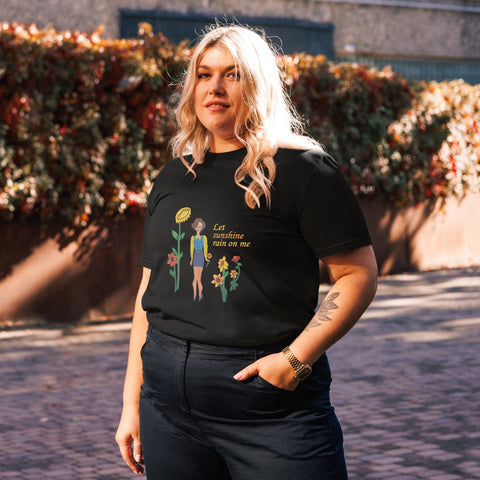 Woman wearing a black t-shirt with a sunflower graphic design and text 'Let sunshine rain on me', standing outdoors.
