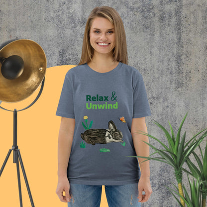 Woman wearing dark heather blue organic cotton t-shirt with hand-painted black-and-white rabbit, butterfly, greens, and "Relax & Unwind" text — front view.