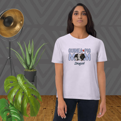 Woman wearing a 'Guinea Pig Mom' t-shirt in lavender with plants and a lamp in the background.