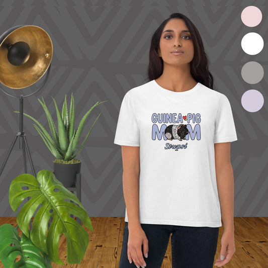 Person wearing a white t-shirt with 'Guinea Pig Mom' design in a room with plants and a lamp.