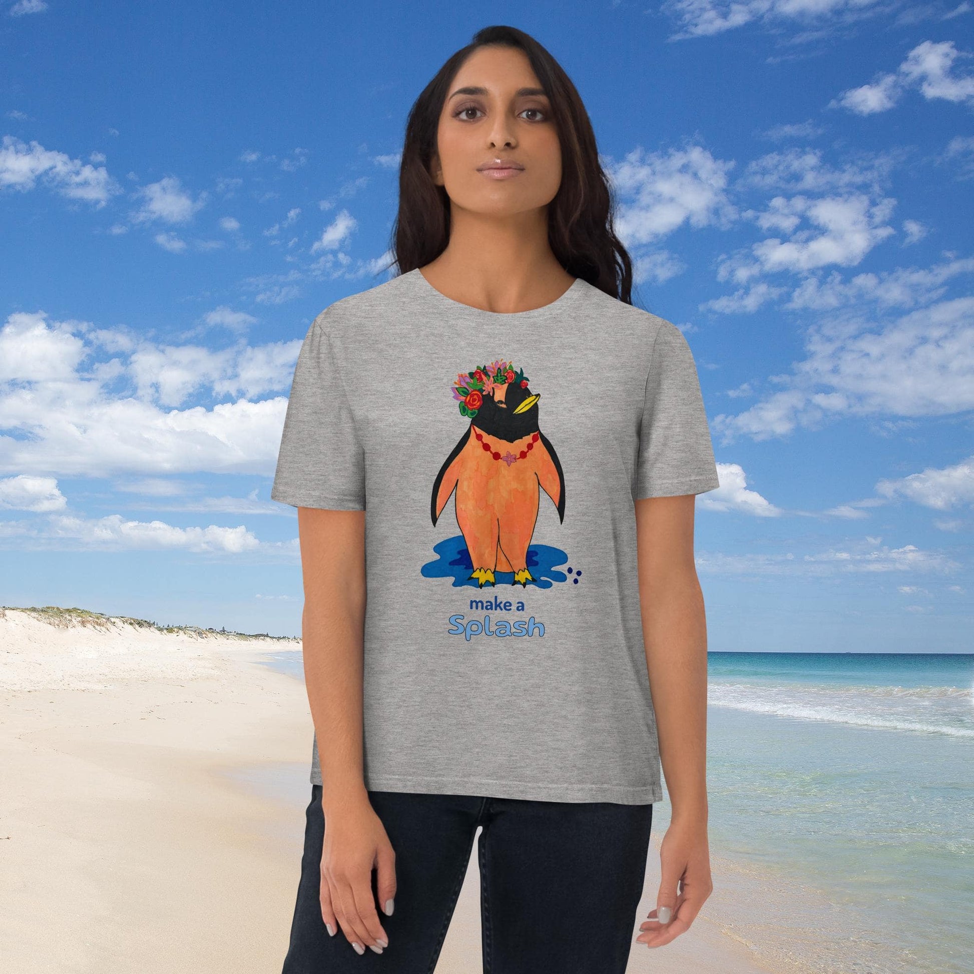 Woman wearing a gray t-shirt with a penguin graphic and the words 'Make a splash' on a beach