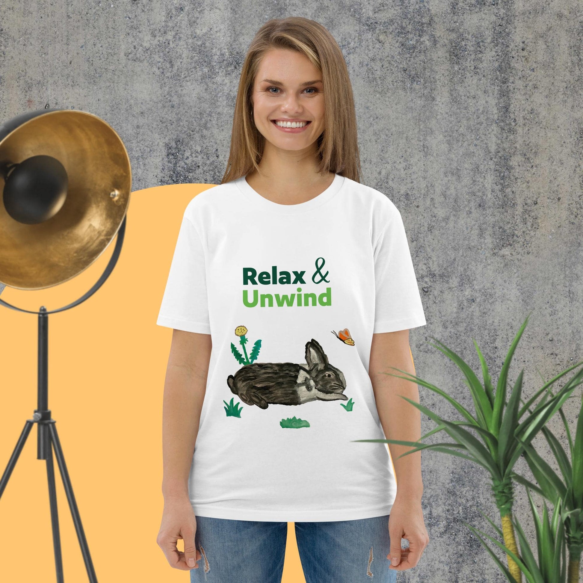 Woman wearing white organic cotton t-shirt with hand-painted black-and-white rabbit, butterfly, greens, and "Relax & Unwind" text — front view.