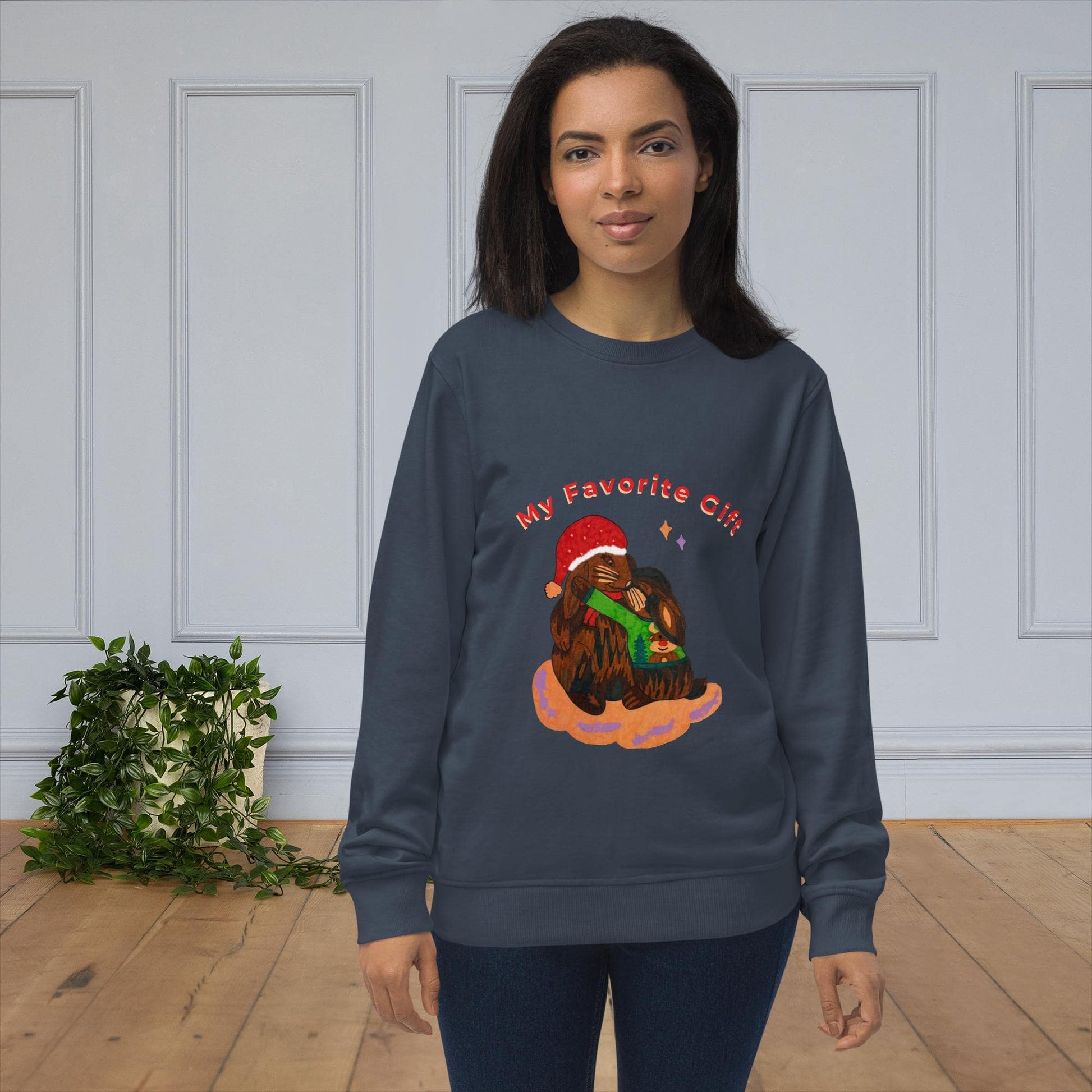 Woman wearing a navy sweatshirt with a rabbit christmas graphic design in a room with white paneled walls and a plant.