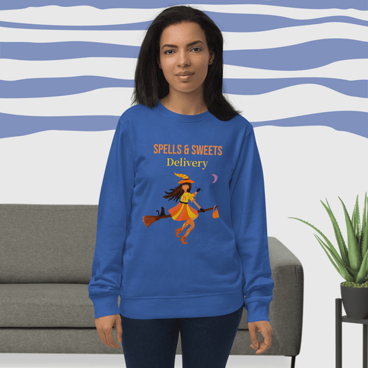 Woman wearing a blue sweatshirt with 'Spells & Sweets Delivery' Halloween design in a living room setting.