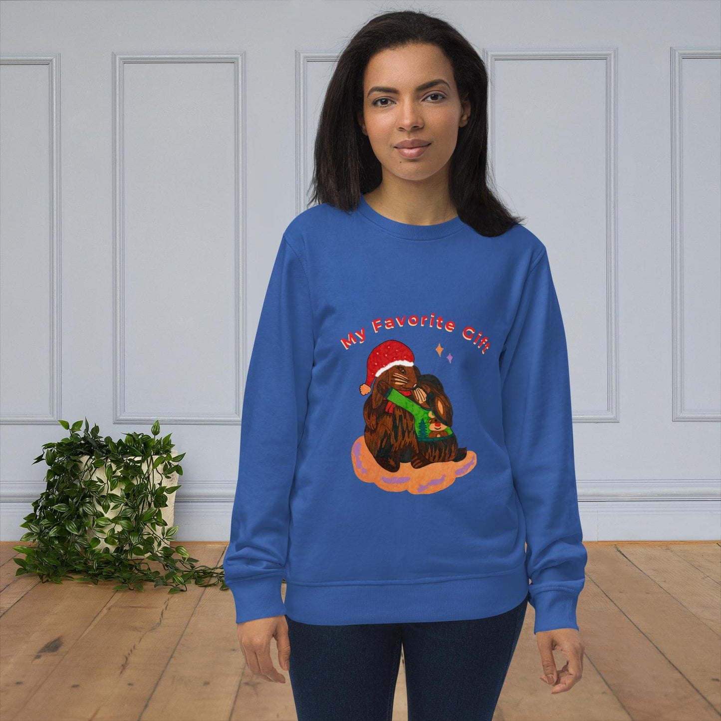Woman wearing a blue sweatshirt with a rabbit design and text 'My favorite gift', standing in a room with a white paneled wall and wooden floor.