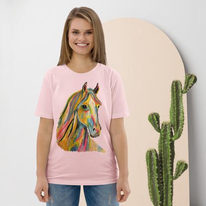 A woman wearing a light pink t-shirt with a colorful watercolor-style horse graphic on the front, paired with blue jeans, standing in front of a beige arched backdrop with a cactus prop.
