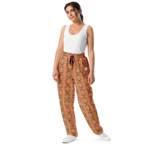 Front view of a woman wearing wide-leg orange joggers with an oak vine and acorn pattern, crafted from eco-friendly recycled polyester.